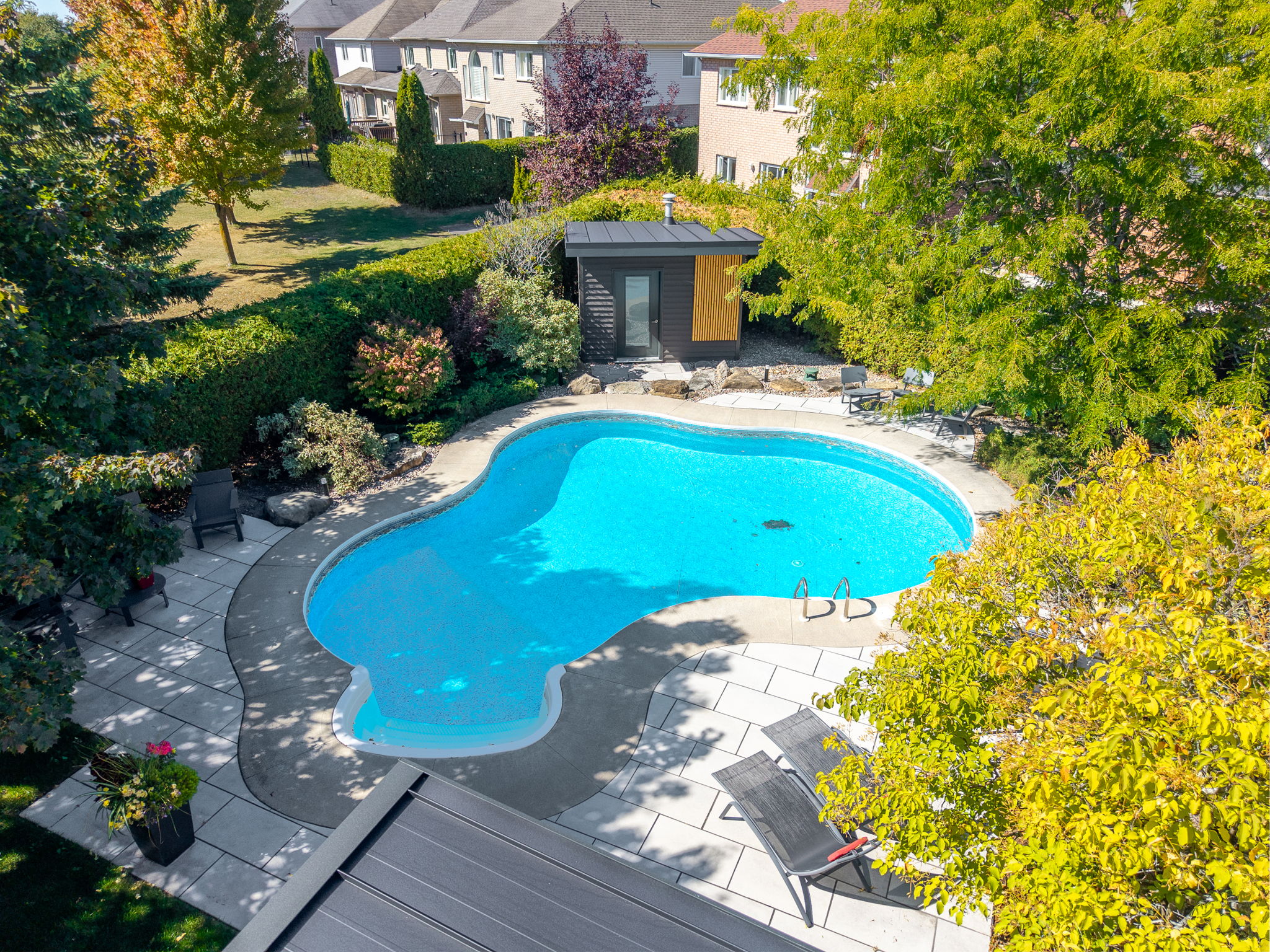 Poolside view of a modern covered lounge and finished hardscape beside a bright blue pool