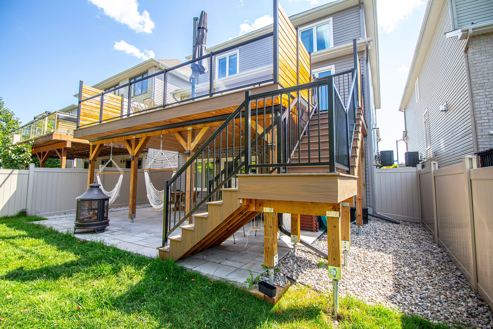 Elevated deck with warm wood framing, black railing, and stairs leading down to a finished patio below.