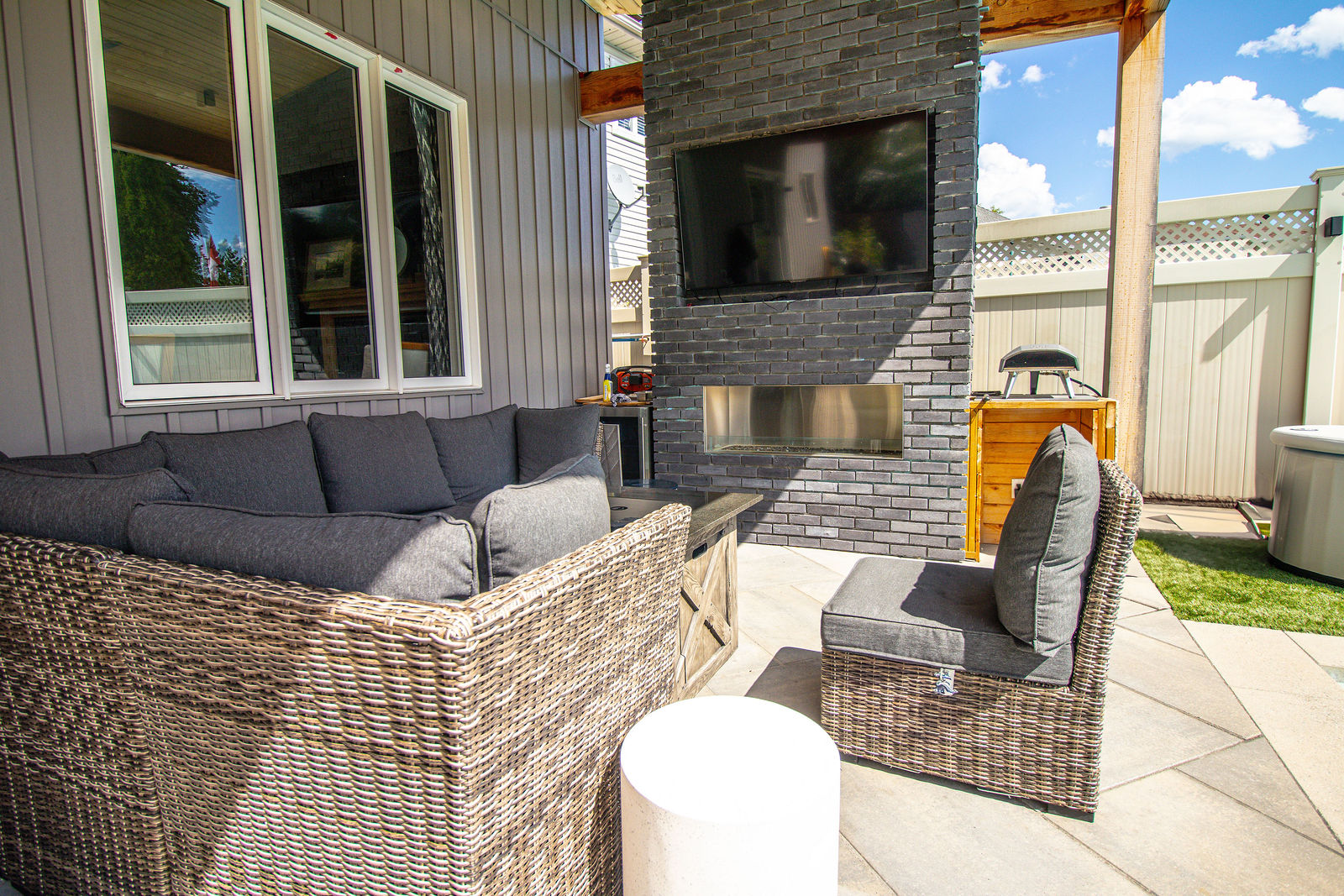 Covered outdoor lounge with woven seating, built-in fireplace wall, and integrated patio beside the pool area.